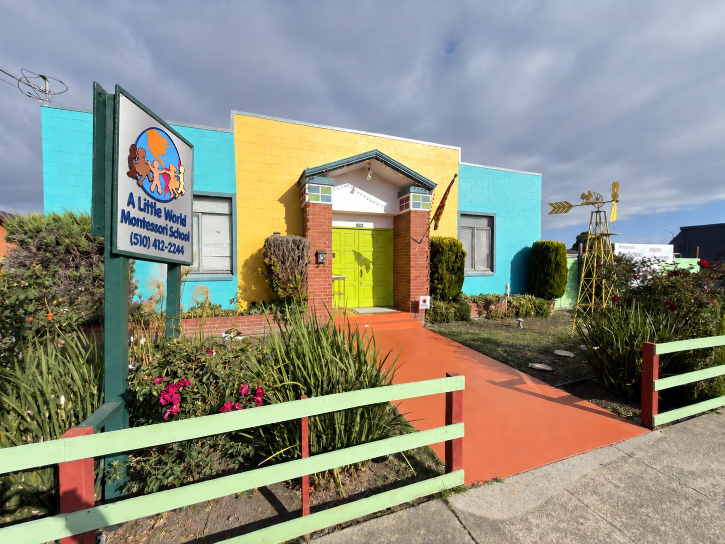 The front of A Little World Montessori behind its cheerful, brightly painted fence, framed by leafy trees